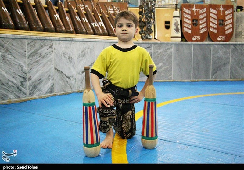 کودک خردسال با لباس پهلوانی و میل‌های زورخانه در سالن ورزش باستانی